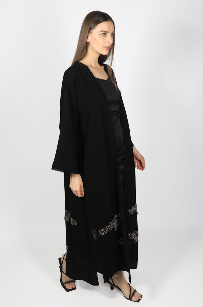 services-06 A woman wearing a stylish black abaya stands against a white backdrop, showcasing Middle Eastern fashion.