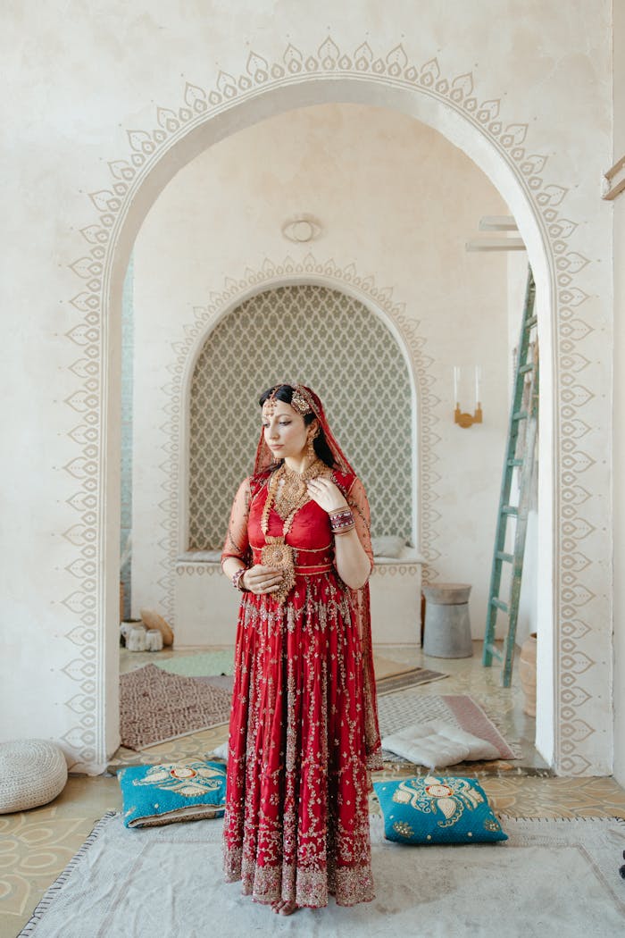 home-hero Indian woman in a red sari standing indoors, adorned with jewelry, showcasing cultural heritage.